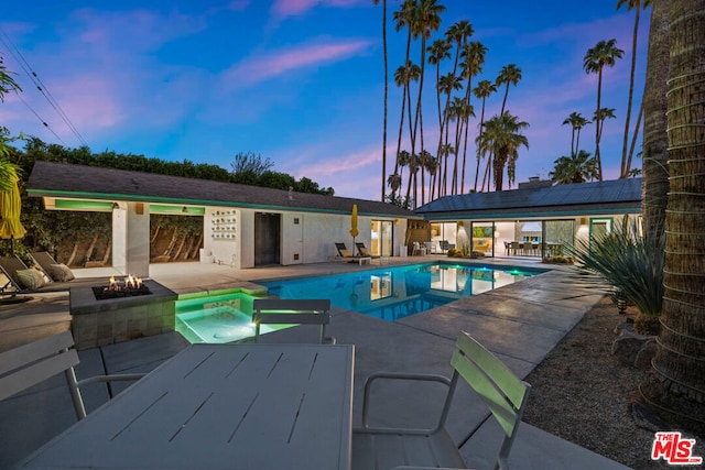 pool at dusk with an in ground hot tub, a patio area, and a fire pit