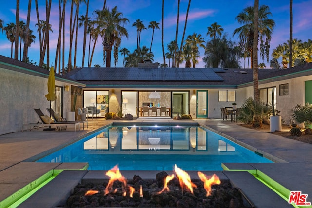 pool at dusk with an outdoor fire pit and a patio