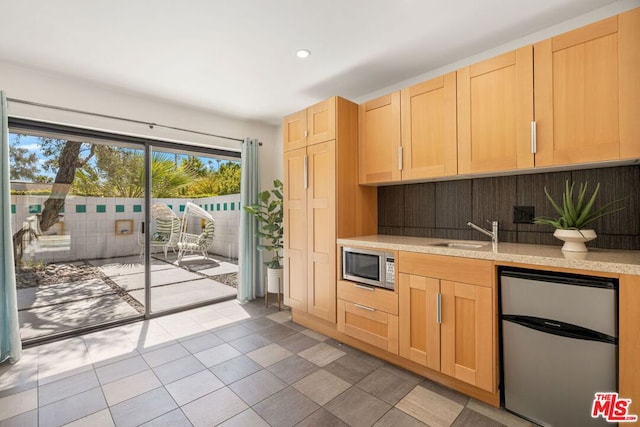 kitchen with appliances with stainless steel finishes, light brown cabinetry, tile patterned flooring, and sink