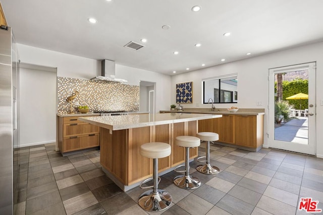 kitchen with a large island, decorative backsplash, wall chimney range hood, a breakfast bar, and sink