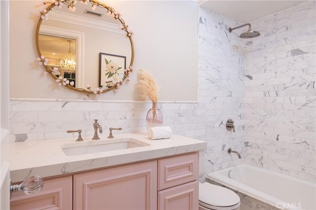 full bathroom with vanity, toilet, tiled shower / bath, and tile walls