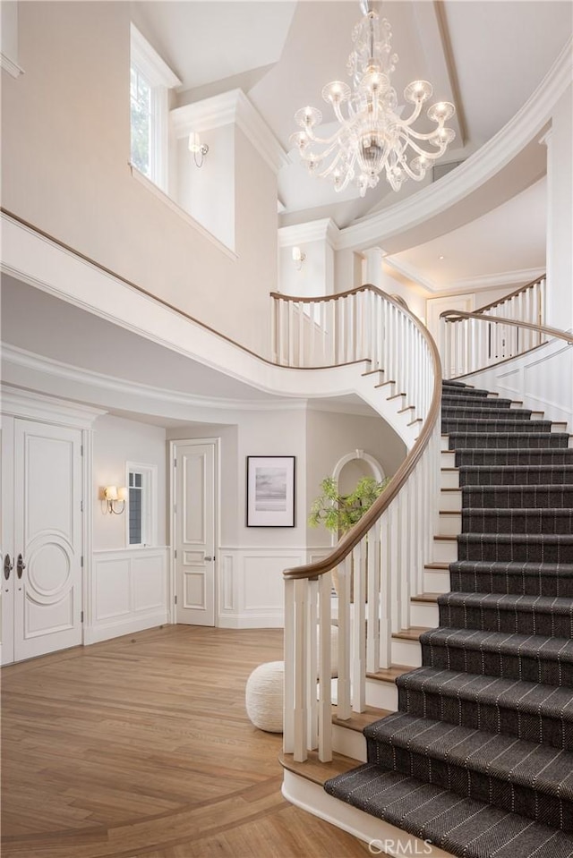 entryway with a high ceiling, light hardwood / wood-style floors, ornamental molding, and a notable chandelier