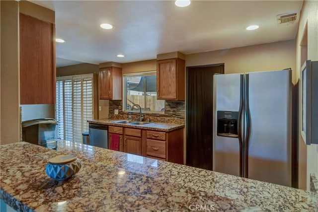 kitchen featuring appliances with stainless steel finishes, sink, decorative backsplash, kitchen peninsula, and light stone countertops