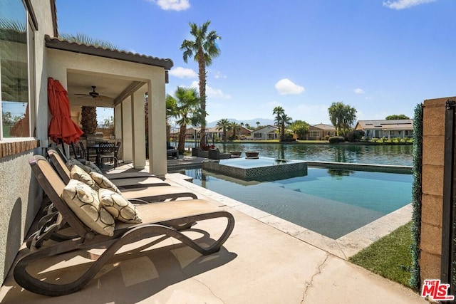 view of swimming pool featuring ceiling fan, a patio, a water view, and an in ground hot tub