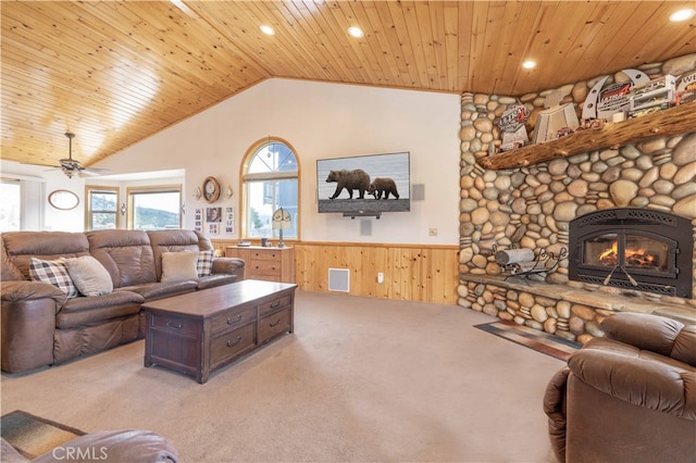 carpeted living room featuring wood walls, a stone fireplace, wood ceiling, and ceiling fan