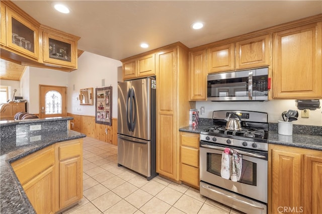 kitchen with light tile patterned flooring, dark stone counters, wooden walls, and stainless steel appliances