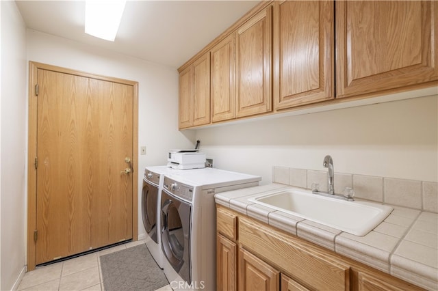 clothes washing area with light tile patterned flooring, washing machine and dryer, cabinets, and sink