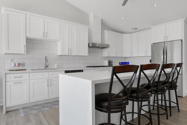 kitchen featuring stainless steel refrigerator, sink, a kitchen breakfast bar, vaulted ceiling, and white cabinets