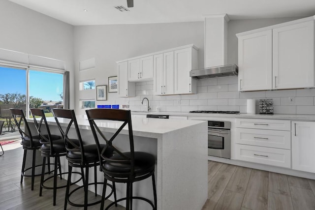 kitchen featuring a center island, stainless steel oven, wall chimney exhaust hood, white cabinets, and light wood-type flooring