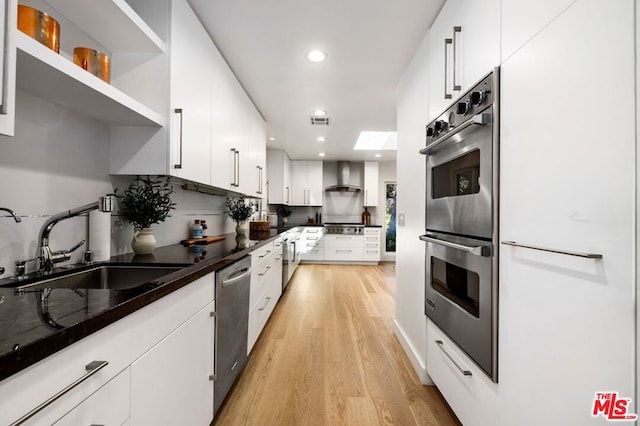 kitchen featuring light wood-type flooring, stainless steel appliances, sink, wall chimney range hood, and white cabinets