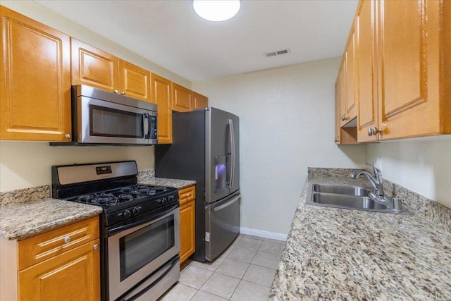 kitchen with appliances with stainless steel finishes, sink, light stone counters, and light tile patterned flooring