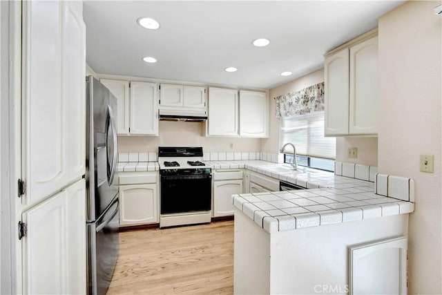 kitchen featuring sink, light hardwood / wood-style flooring, tile countertops, stainless steel fridge, and white gas range oven