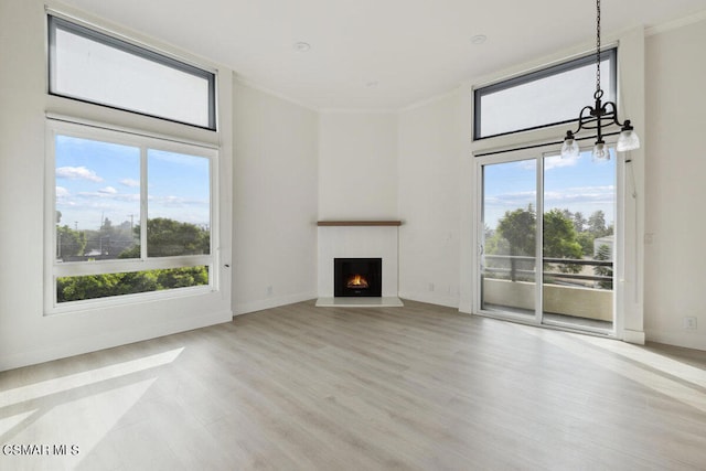 unfurnished living room featuring an inviting chandelier, ornamental molding, and light wood-type flooring