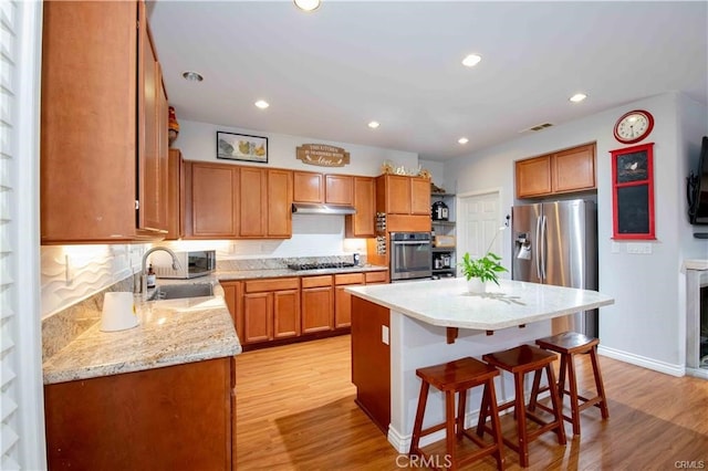 kitchen with light hardwood / wood-style floors, a kitchen island, sink, decorative backsplash, and appliances with stainless steel finishes