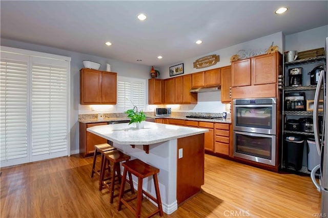 kitchen with appliances with stainless steel finishes, a breakfast bar area, a center island, and light hardwood / wood-style flooring