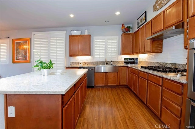 kitchen with extractor fan, a kitchen island, light hardwood / wood-style flooring, sink, and appliances with stainless steel finishes