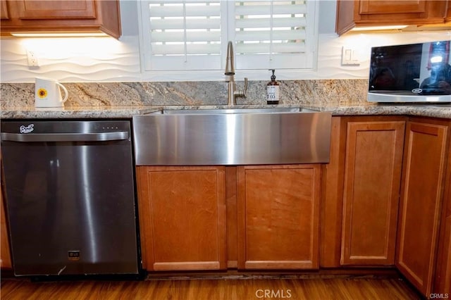 kitchen with stainless steel appliances, light stone countertops, light hardwood / wood-style floors, and sink