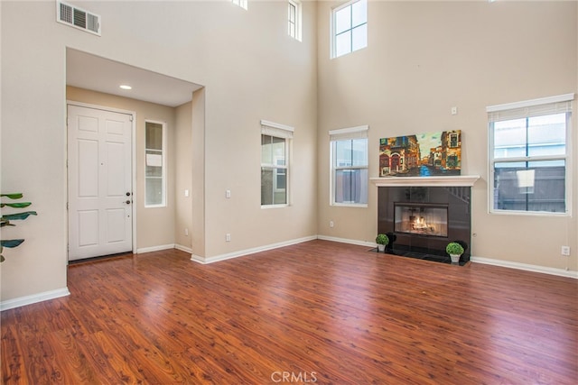 unfurnished living room featuring wood finished floors, visible vents, baseboards, a high ceiling, and a tiled fireplace