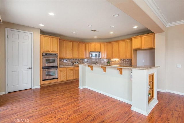 kitchen featuring wood finished floors, visible vents, stainless steel appliances, a kitchen bar, and tasteful backsplash