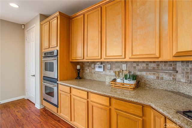 kitchen with light stone counters, baseboards, stainless steel double oven, decorative backsplash, and dark wood-type flooring