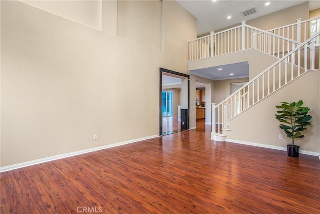 unfurnished living room featuring visible vents, wood finished floors, stairway, baseboards, and a towering ceiling