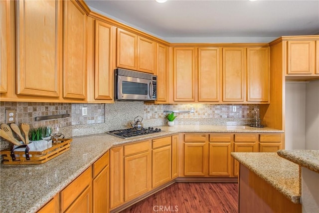 kitchen with light stone counters, backsplash, appliances with stainless steel finishes, and dark wood-style floors