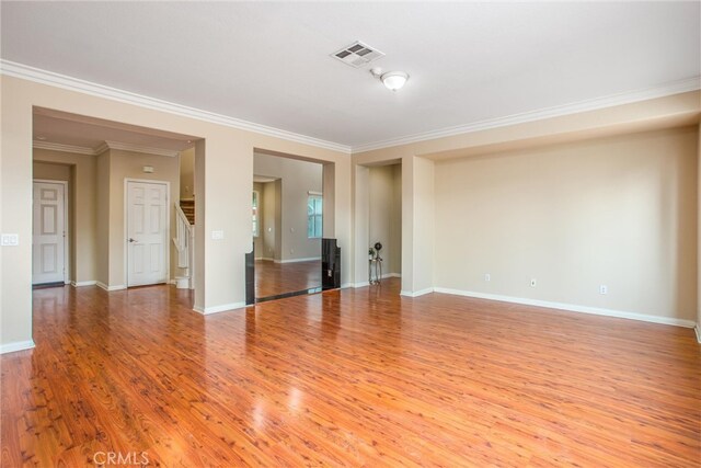 unfurnished living room with visible vents, wood finished floors, stairway, crown molding, and baseboards