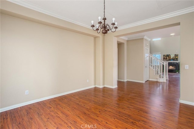 spare room with a chandelier, baseboards, wood finished floors, and crown molding