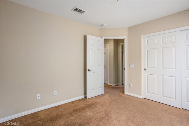 unfurnished bedroom with light carpet, visible vents, a closet, and baseboards