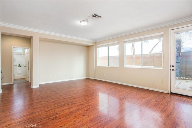 spare room featuring visible vents, a healthy amount of sunlight, wood finished floors, and ornamental molding