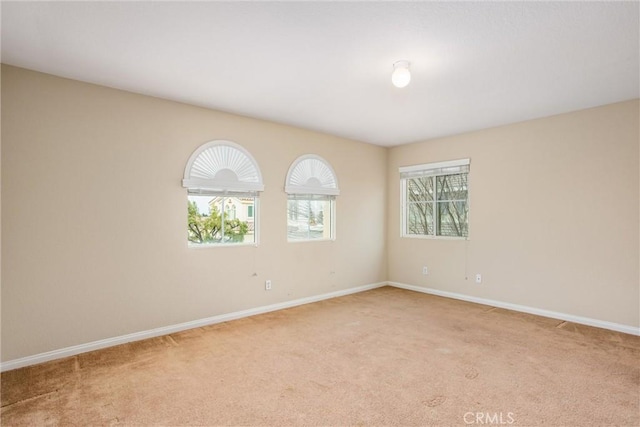 spare room featuring a wealth of natural light, light carpet, and baseboards