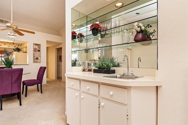 bar with ceiling fan, sink, white cabinets, and light colored carpet