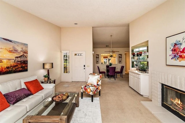 living room featuring a fireplace, ceiling fan, a towering ceiling, and light carpet