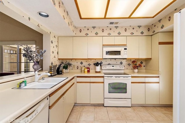 kitchen with light tile patterned floors, white appliances, cream cabinets, and sink