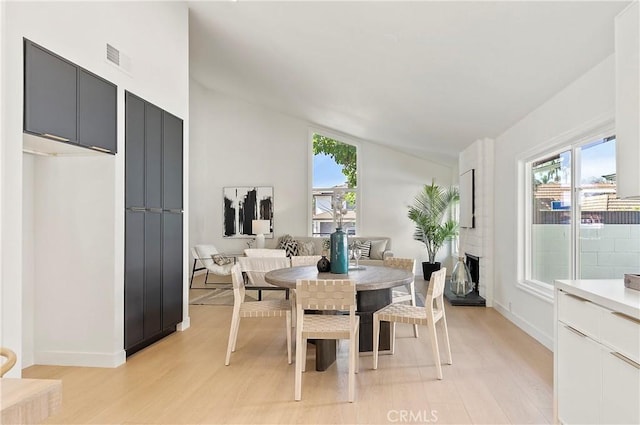 dining space featuring light hardwood / wood-style floors, a fireplace, and vaulted ceiling