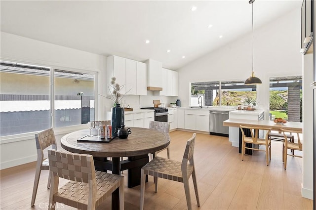 dining space with light wood-type flooring, sink, and high vaulted ceiling