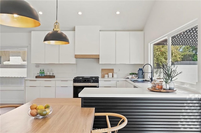 kitchen with stainless steel gas stove, sink, pendant lighting, vaulted ceiling, and white cabinets