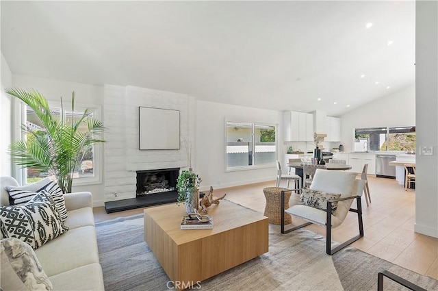 living room featuring a large fireplace, lofted ceiling, sink, and light hardwood / wood-style flooring