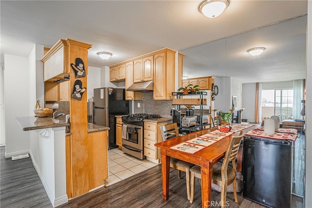 kitchen with light wood-type flooring, decorative backsplash, black refrigerator, stainless steel range with gas cooktop, and light brown cabinetry