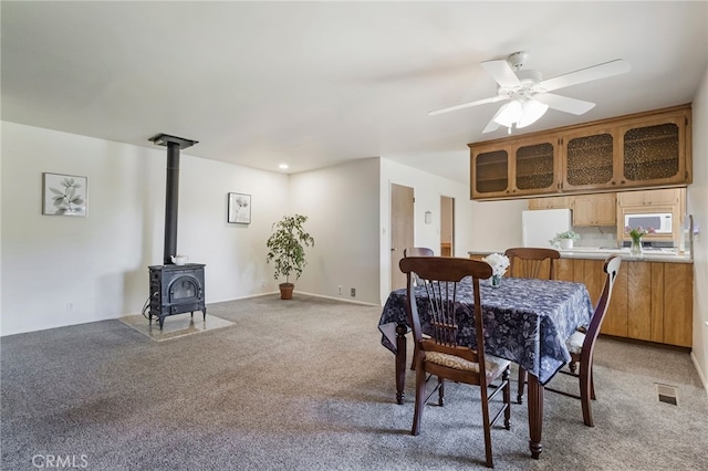 carpeted dining room featuring ceiling fan and a wood stove