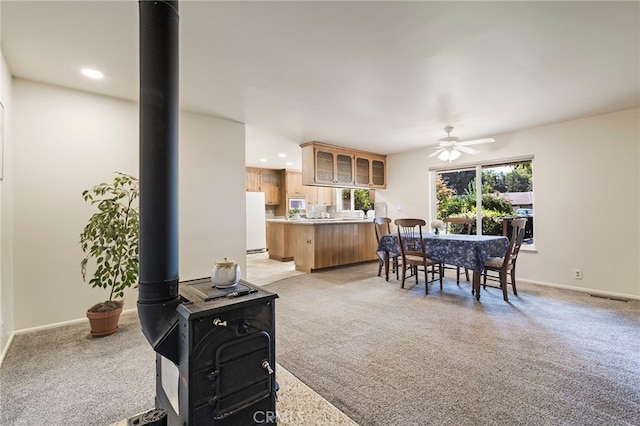 carpeted dining space featuring ceiling fan and a wood stove