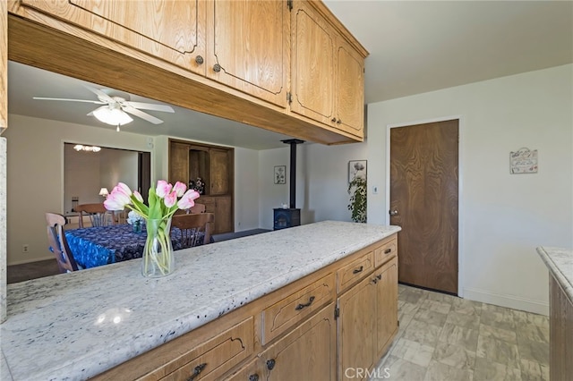 kitchen featuring ceiling fan, a wood stove, and light stone counters