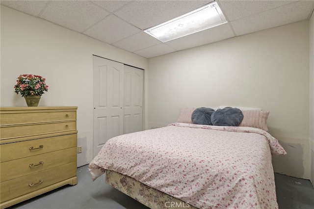 bedroom featuring a closet, concrete flooring, and a drop ceiling