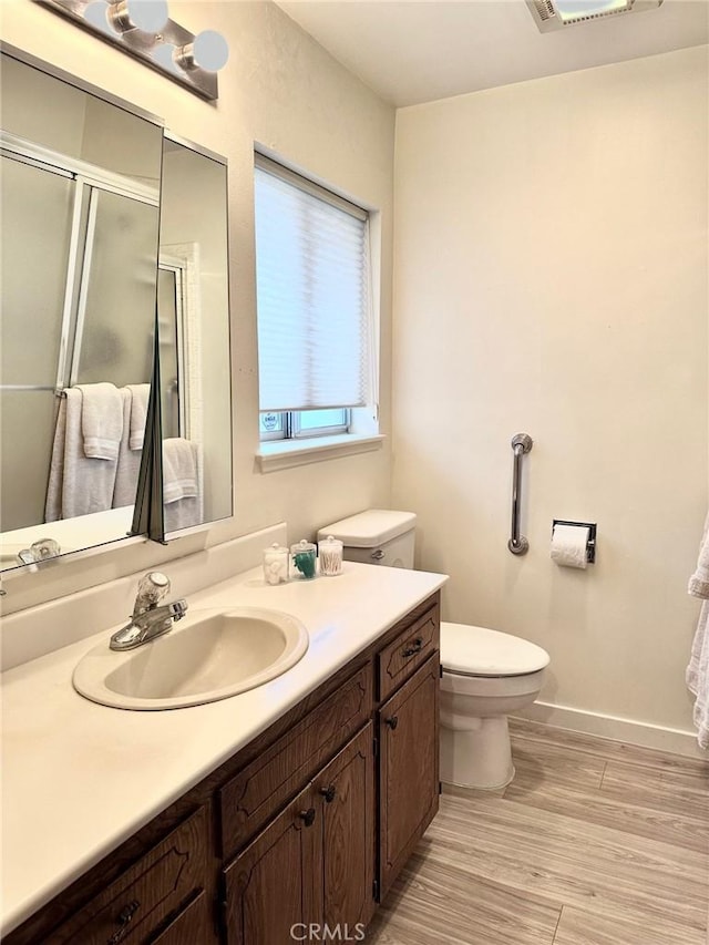 bathroom with toilet, a shower with shower door, hardwood / wood-style flooring, and vanity