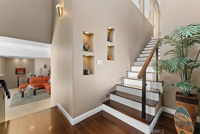 stairway with a high ceiling, built in features, and hardwood / wood-style floors