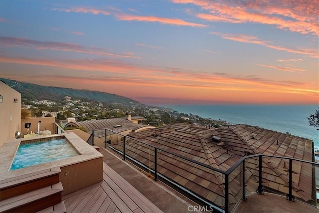 deck at dusk with a jacuzzi and a water and mountain view