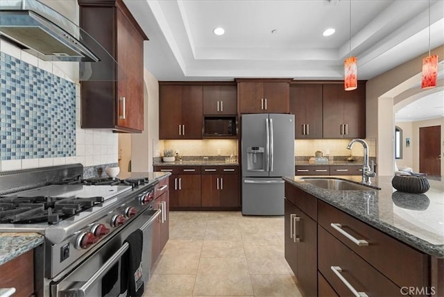 kitchen featuring wall chimney range hood, stainless steel appliances, decorative backsplash, sink, and hanging light fixtures