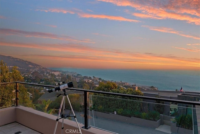 balcony at dusk featuring a water view