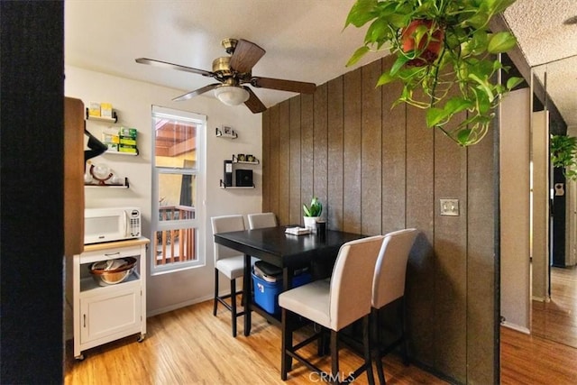 dining space with light hardwood / wood-style flooring, ceiling fan, and wood walls