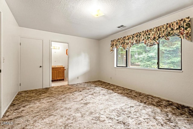 unfurnished bedroom with carpet floors, a textured ceiling, and connected bathroom